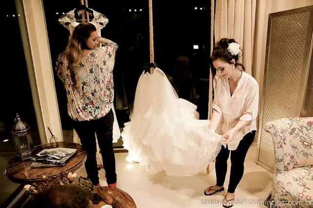 Adriana ajustando a saia de um vestido de noiva durante uma prova no ateliê